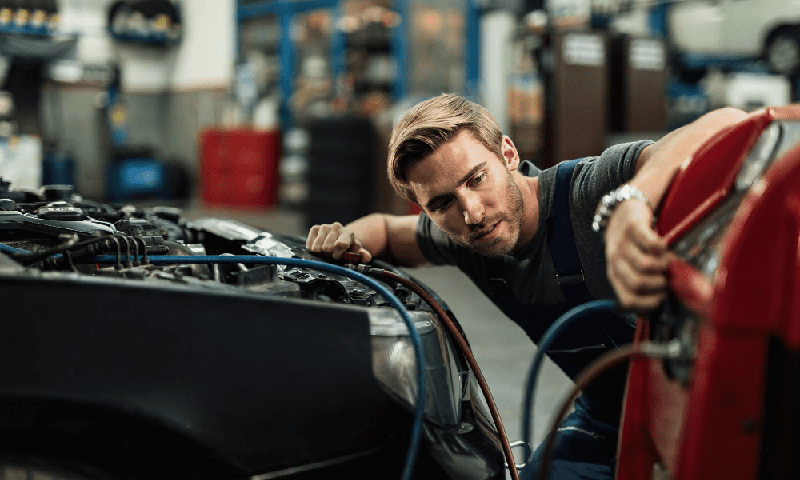 young auto mechanic using compressor while maintaining ac unit of a car at workshop